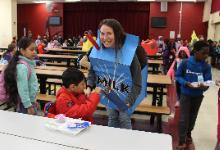 Lunch employee dressed as a carton of milk hands out pencils to smiling children