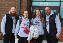 Two girls wrestling team members smile with their coaches outside high school.
